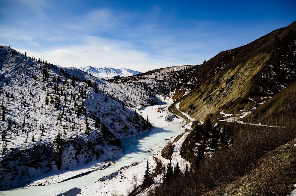 Aerial view of a snow-covered mountainous terrain with a partially frozen river in Burwash Landing, Yukon.